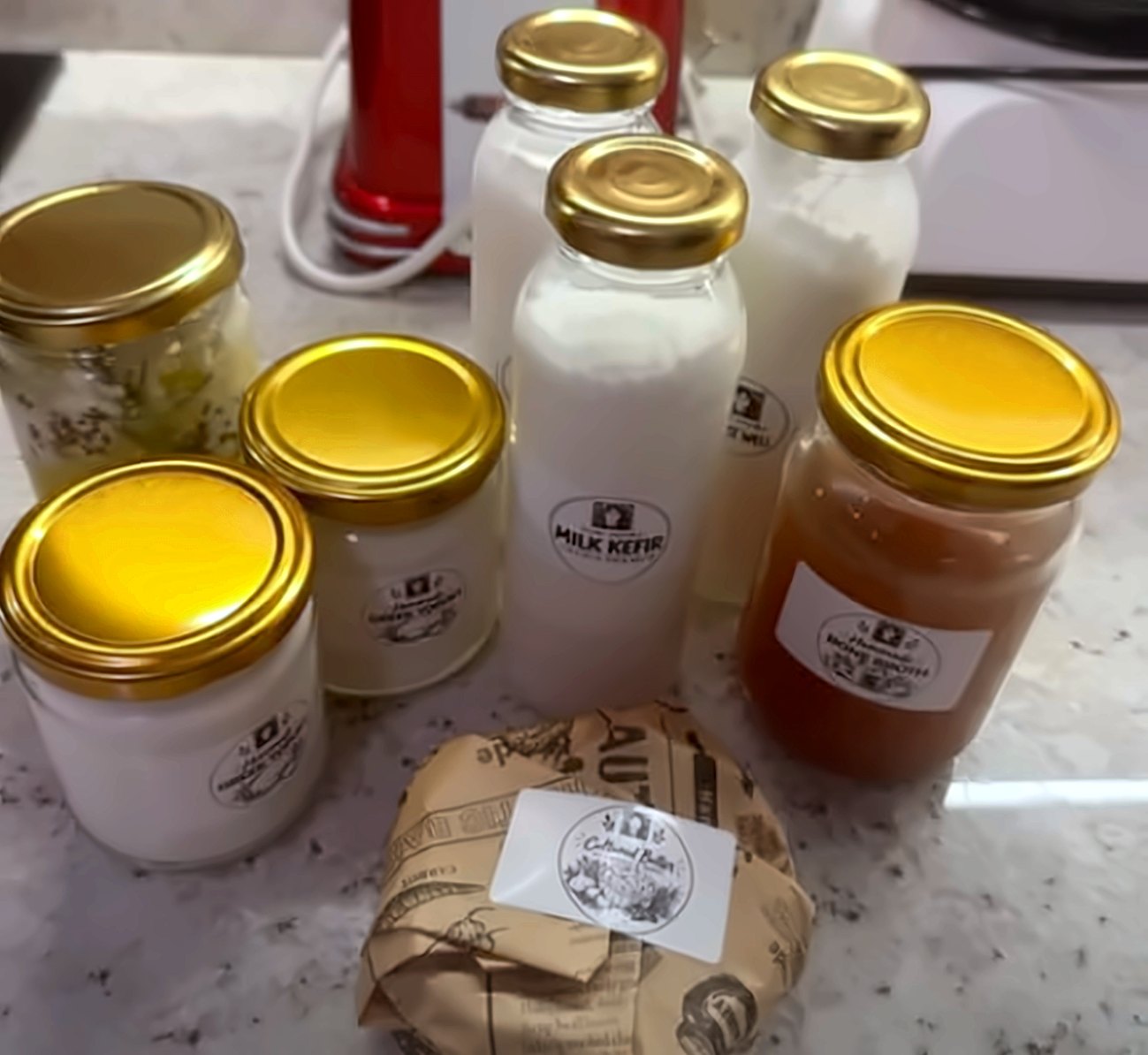 Mai Cooks jars on a kitchen counter: Greek yogurt, milk kefir bottles, bone broth and cultured butter wrapped in paper